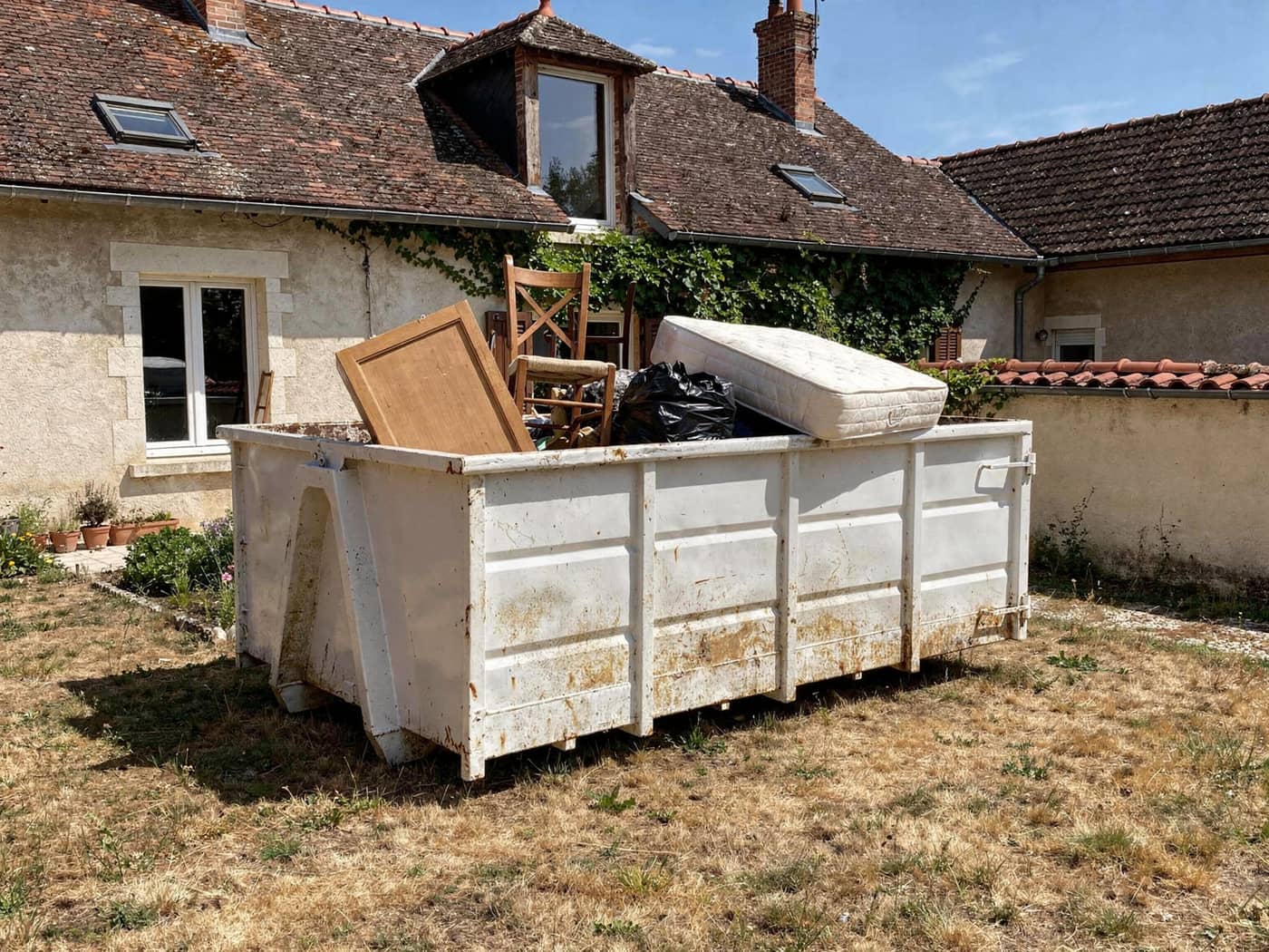 Benne de débarras remplie de meubles devant une maison à Vénissieux