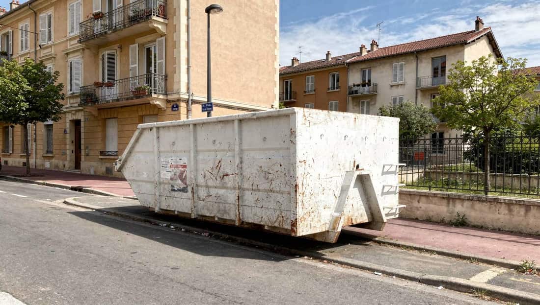 Location de benne à Villeurbanne, benne blanche posée le long du trottoir devant un immeuble